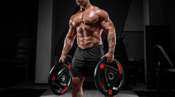 Muscular man stands in a gym with barbell discs. Bodybuilding and powerlifting concept.