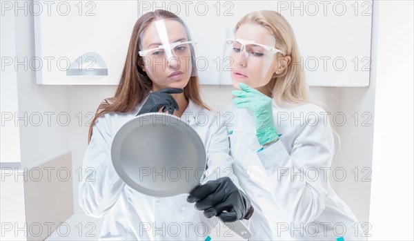 Two beauticians pose in a medical salon with a mirror in their hands. Rejuvenation concept.