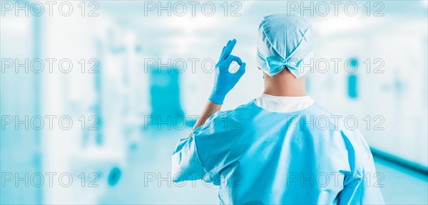 Portrait of a doctor in a clinic. He shows an ok sign. The view from the back. Medicine concept.
