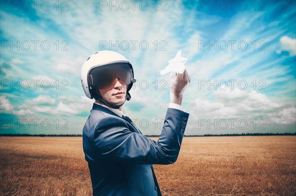 Portrait of a man in a helmet of a pilot. He stands in a field and launches a paper airplane. Business concept.