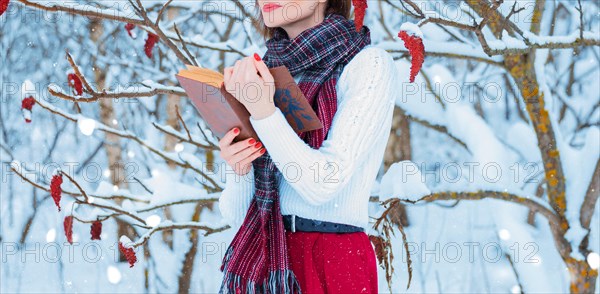 Portrait of a charming girl who reads a book in the winter forest. Concept of Christmas