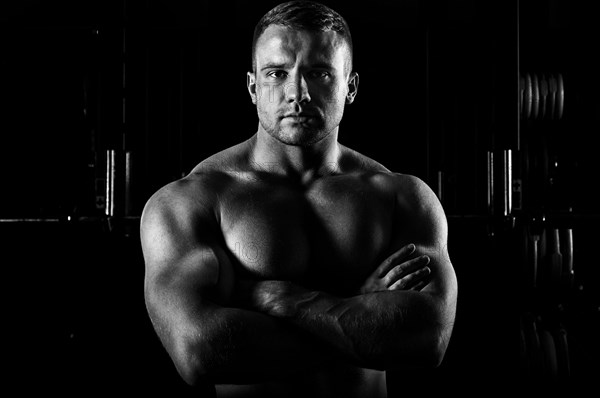 The weightlifter is posing in front of the camera with his arms crossed over his chest. Front view