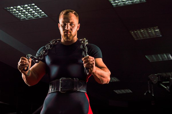 Huge weightlifter with a chain around his neck is in the gym