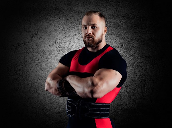 The weightlifter stands in a menacing pose with crossed huge arms and looks at the camera