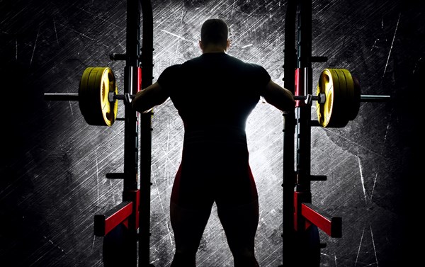 The weightlifter stands with his hands behind the heavy barbell. Back view