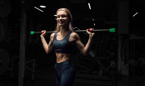 Charming blonde posing in the gym with a body-bar. Front view. The concept of sports