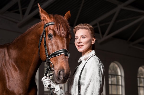 Portrait of a stylish woman hugging a thoroughbred horse. Love and care concept.