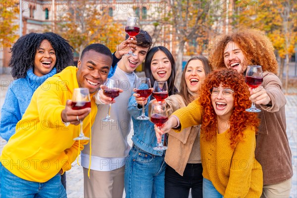 Multi-ethnic young people smiling and toasting with wine to the camera in the street
