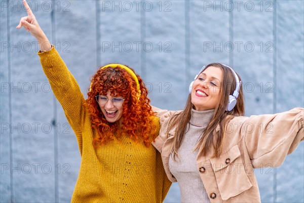 Happy female friends listening to music with headphones in the street