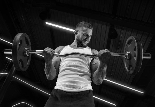 Handsome young man working out with a barbell in the gym. Biceps pumping. Fitness and bodybuilding concept.