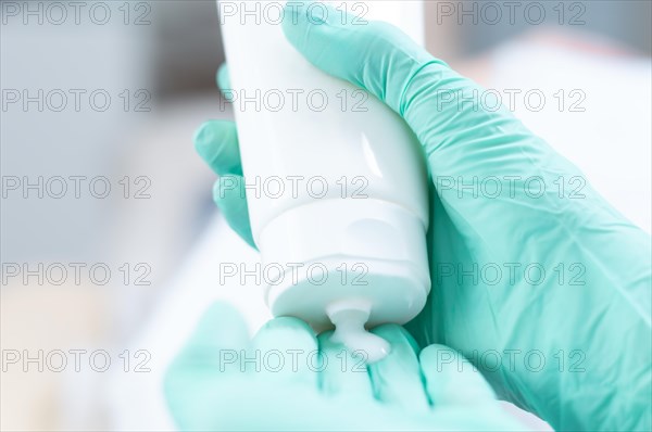 Picture of hands in medical gloves squeezing cream out of a white tube. Skin care concept.