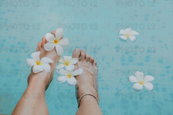 Feet adorned with plumeria flowers by a blue swimming pool