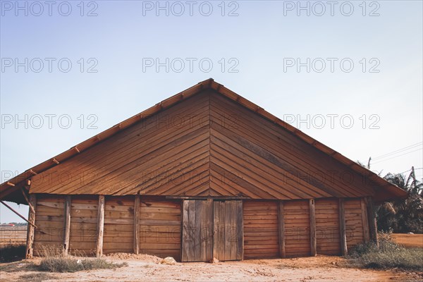 Front view of a wooden barn with a gable roof under a clear sky. Kampot