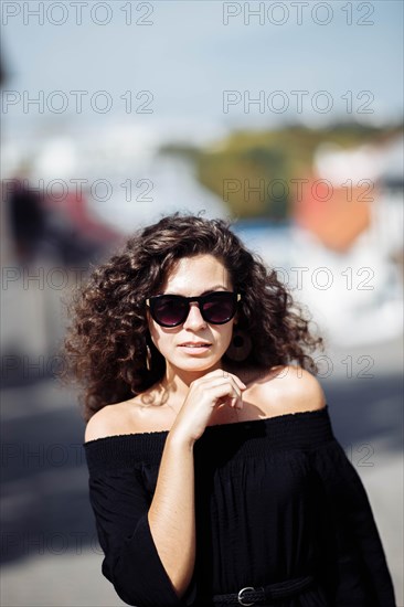 Portrait of a stylish beautiful young curly woman in a black dress and sunglasses