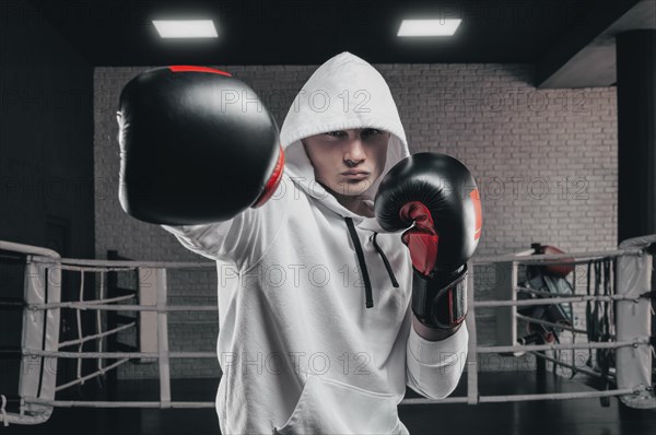 Brutal athlete boxing in the ring in a white hoodie covered with a hood. Mixed martial arts concept. High image quality