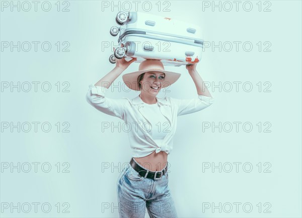 Portrait of an attractive woman in a huge hat carrying a suitcase on her head. Travel concept.