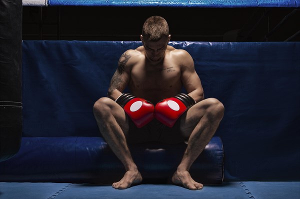 Boxer sits in gloves near the ring with his head bowed. The concept of sports