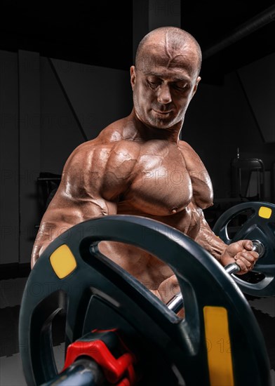 Professional weightlifter posing in the gym with a barbell in his hands. Classic bodybuilding.