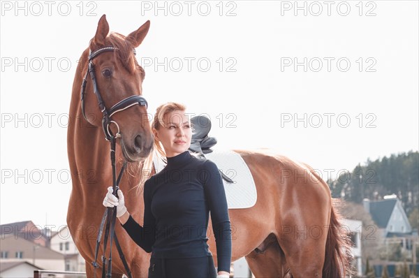 Beautiful stylish woman walking with a horse in a country club. Equestrian sport