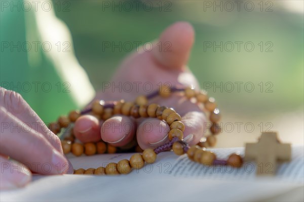 A woman's hands praying the rosary in the field over an open bible on a wooden table