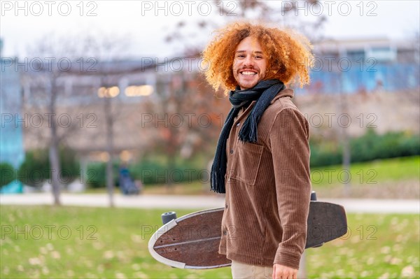Portrait of an alternative man with skateboard smiling at camera standing on a park