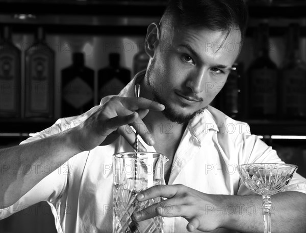 Charming bartender prepares a cocktail in a mixing bowl.