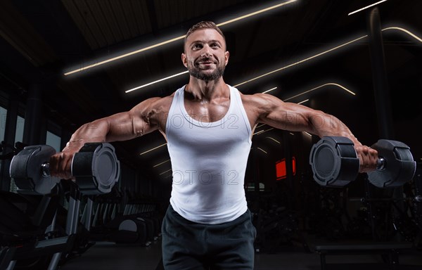 Handsome young man spreads his arms with dumbbells to the sides. Shoulder pumping. Fitness and bodybuilding concept.