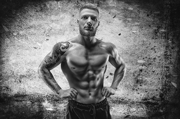 Young muscular guy with handsome abs posing against the backdrop of a concrete wall. Fitness and nutrition concept.