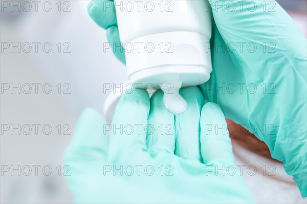 Picture of hands in medical gloves squeezing cream out of a white tube. Skin care concept.