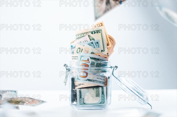 Glass piggy bank full of money. Banknotes are strewed from above. The concept of squandering.