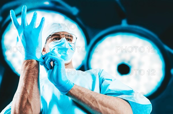Portrait of a doctor on the background of surgical lamps. He pulls on the glove. Medicine concept.