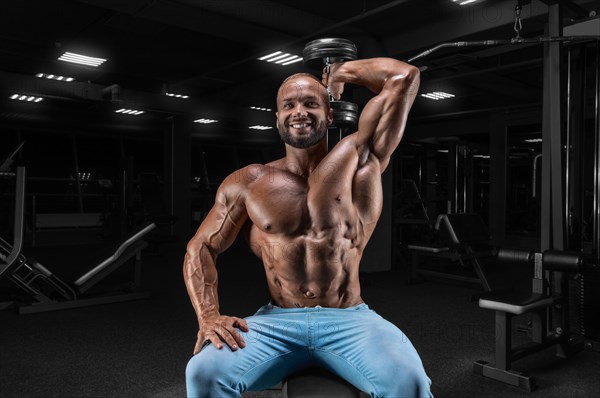 The athlete is doing the exercise in the gym. Lifting a dumbbell with one hand from behind the head. Fitness