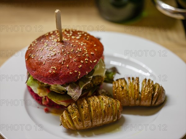 Delicious veggie burger in a beetroot bun with sliced potatoes