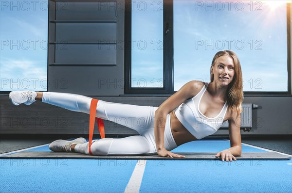 Charming girl lies on the floor and does stretching with elastic. The concept of fitness