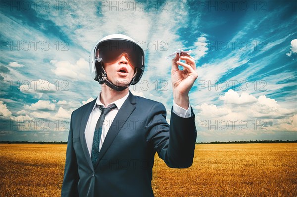 Portrait of a man in a helmet of a pilot. He stands in a field and launches a paper airplane. Business concept.