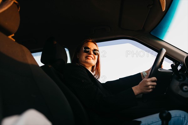 Young beautiful stylish girl driver in a jacket and sunglasses driving a car