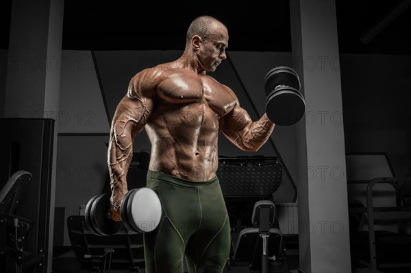 Professional weightlifter is training in the gym. Dumbbell Curl. Bodybuilding concept.