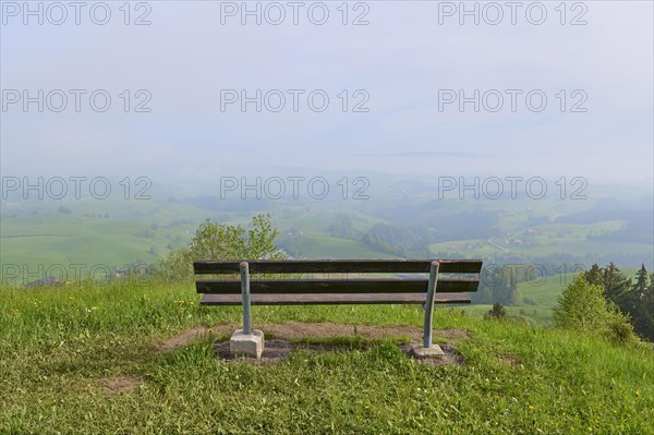 An empty bench stands in a meadow with a view of the mist-covered hills