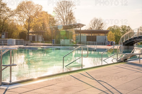 Calm water in an outdoor pool surrounded by railings in low sun