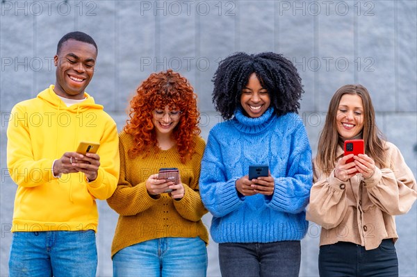 Frontal portrait of smiling young diverse people using phone standing outdoors