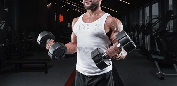 Portrait of a man in a white T-shirt exercising in the gym with dumbbells. Biceps pumping. Fitness and bodybuilding concept.