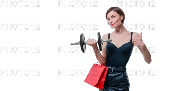 Beautiful slender woman posing in the studio with a dumbbell and gift bags. Gift concept. Gym membership. Ok sign