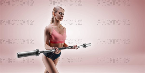 Charming tall sportswoman posing in the studio on a pink background with a barbell in her hands. The concept of sports