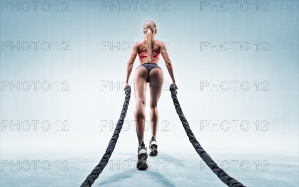 Sports girl trains with ropes. Back view. The concept of sports