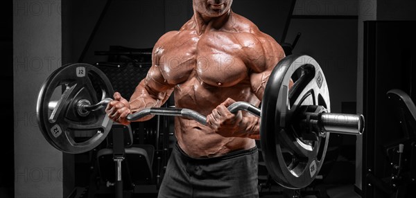 Powerful bodybuilder trains in a gym with a barbell. No name portrait. Bodybuilding concept.