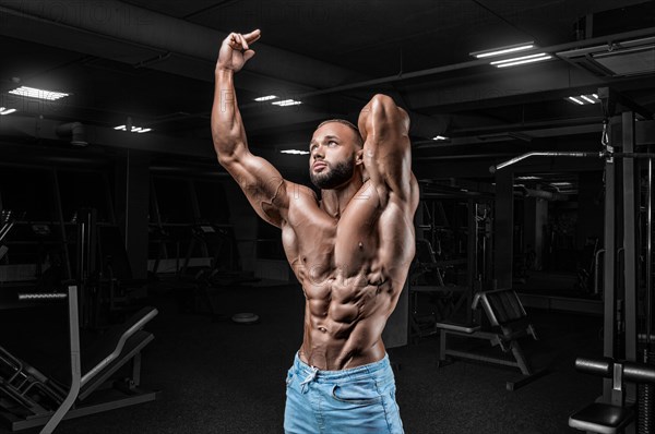 Muscular man in jeans poses in the gym. Sports