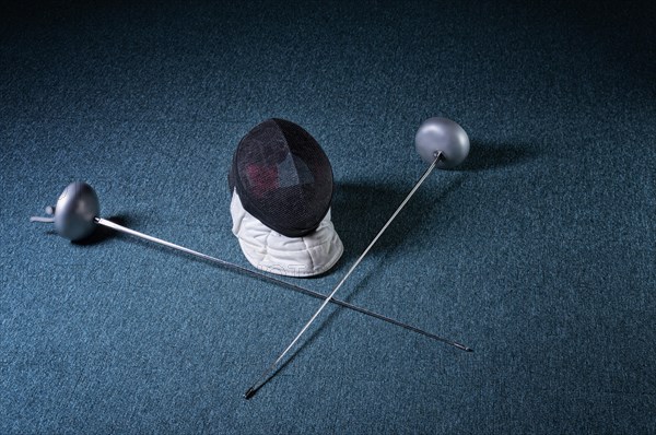 Two swords and mask lie on a blue background. The concept of fencing.