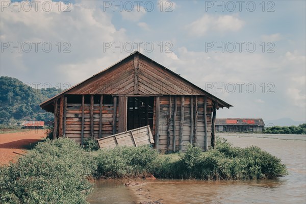 Derelict wooden shack on the riverbank surrounded by greenery. Kampot