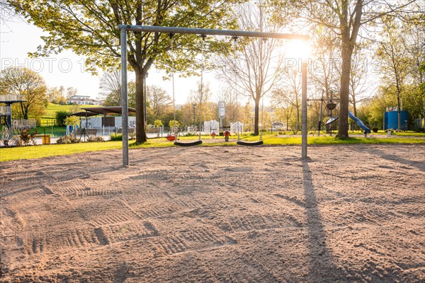 Swing set on sandy ground in the evening light with trees in the background