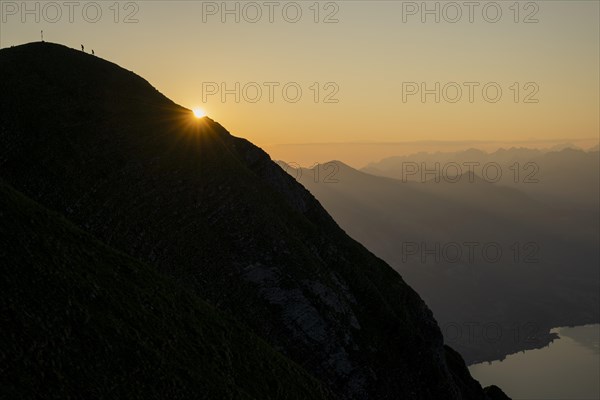 Mountain ridge with mountaineers and Swiss mountains and Lake Thun in the background at sunrise